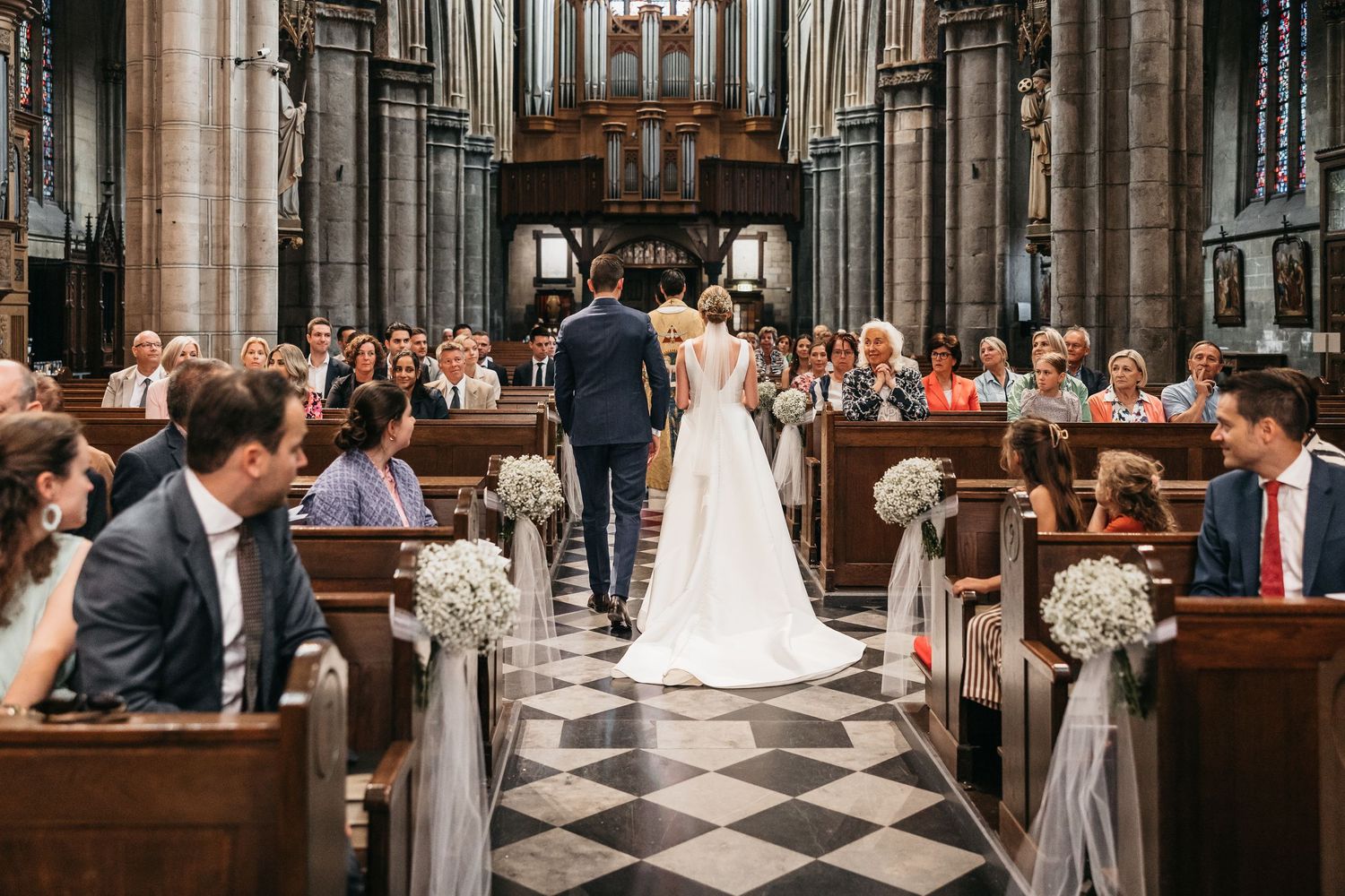 Wedding couple walking down aisle of grand Gothic church with guests seated in decorated pews.