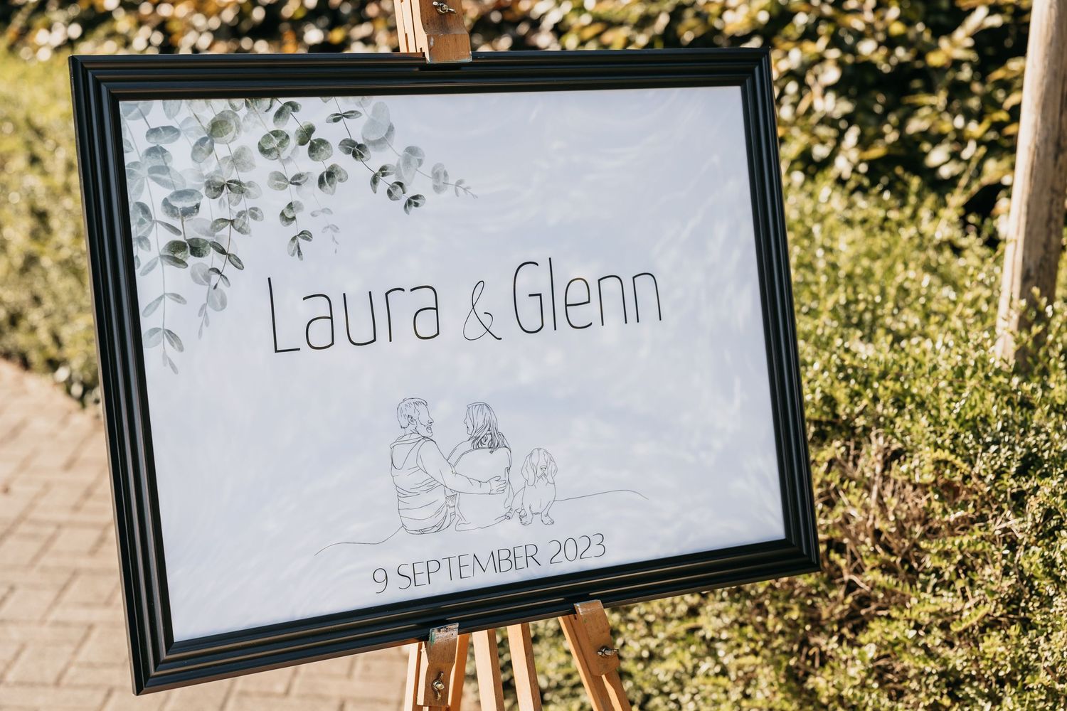 Elegant wedding welcome sign for Laura and Glenn dated 9 September 2023 on an easel outdoors.