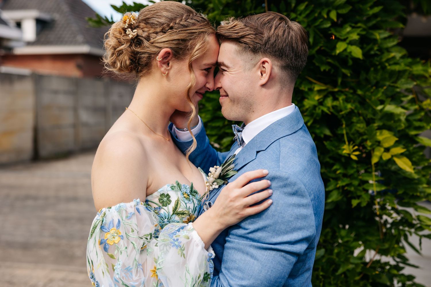 Smiling newlyweds share a joyful moment together, bride in off-shoulder floral dress and groom in blue suit.