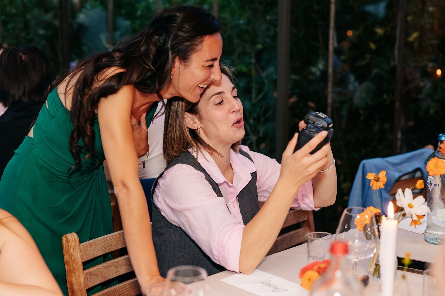 Two women at a wedding reception admiring photos on a camera at a decorated table.
