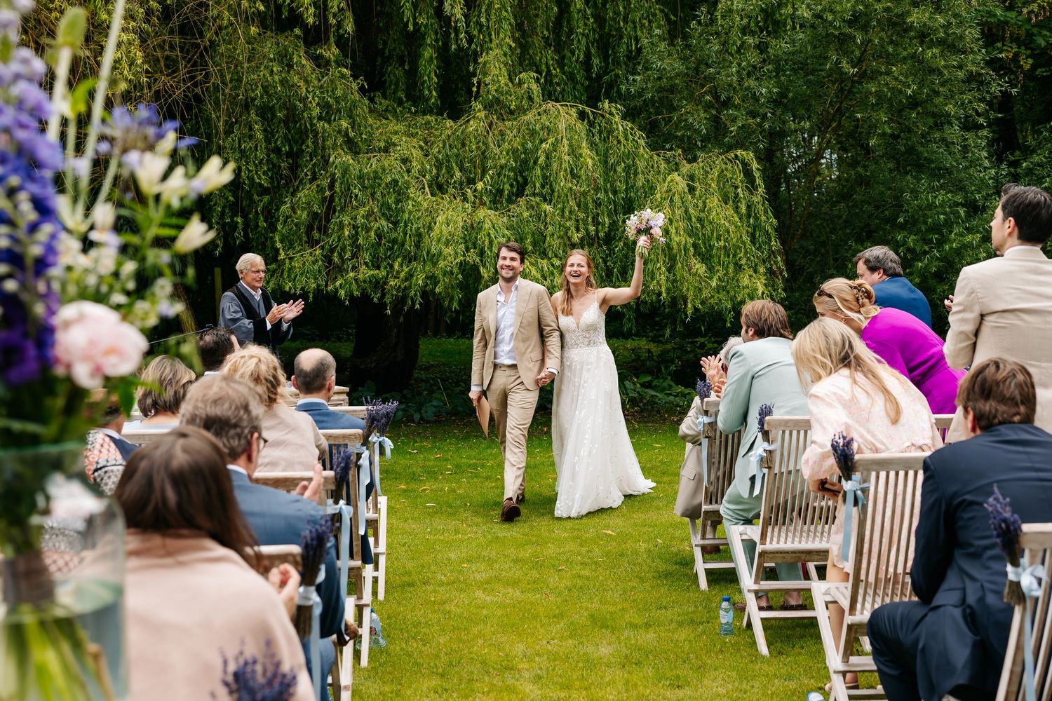 Happy newlyweds walk back down the aisle after outdoor garden wedding ceremony as guests cheer.