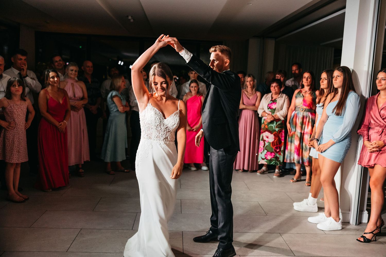 Bride and groom share first dance as wedding guests watch and celebrate at elegant indoor reception.
