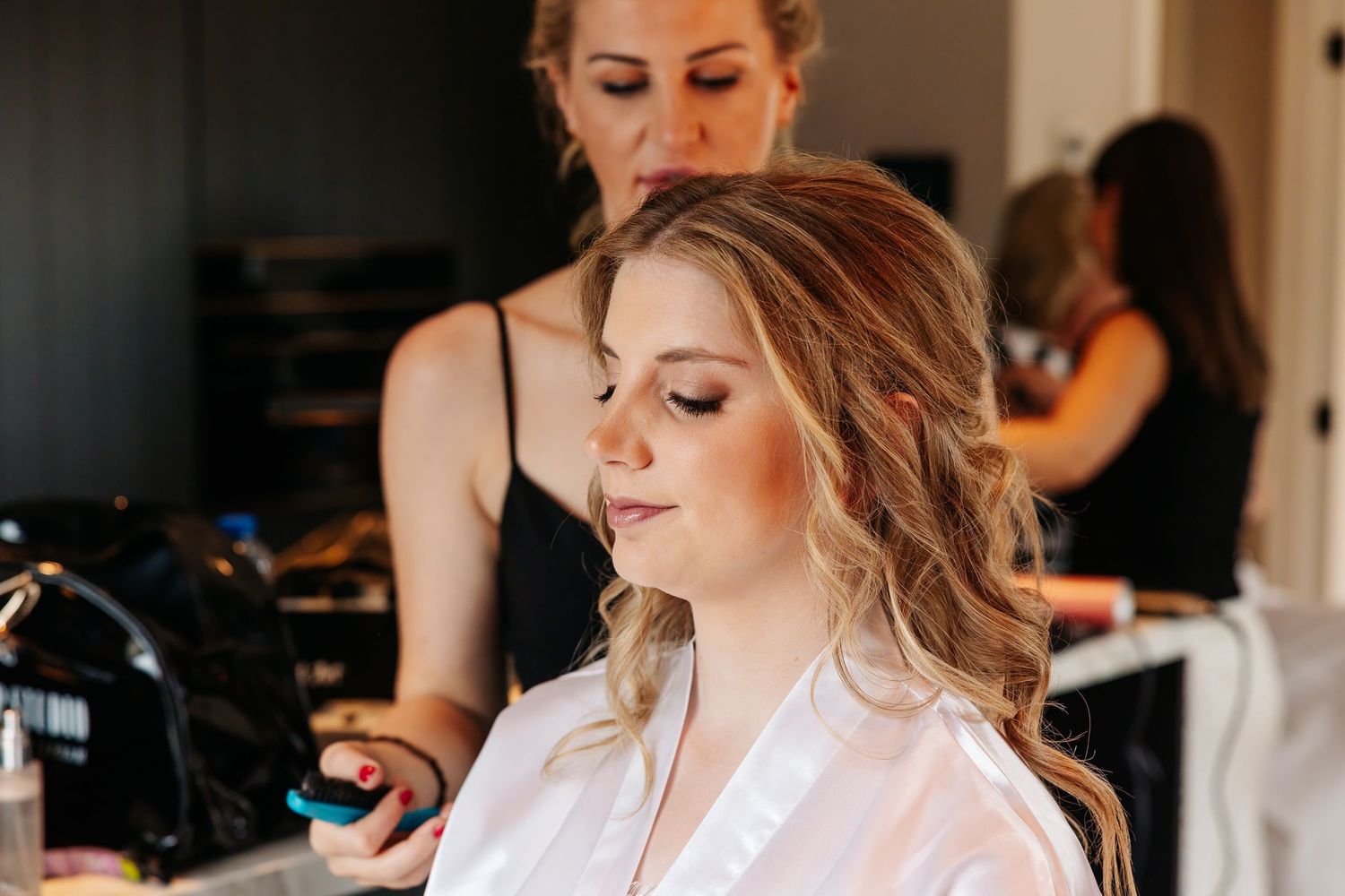 Professional stylist applying finishing touches to bride's makeup during wedding morning preparations.