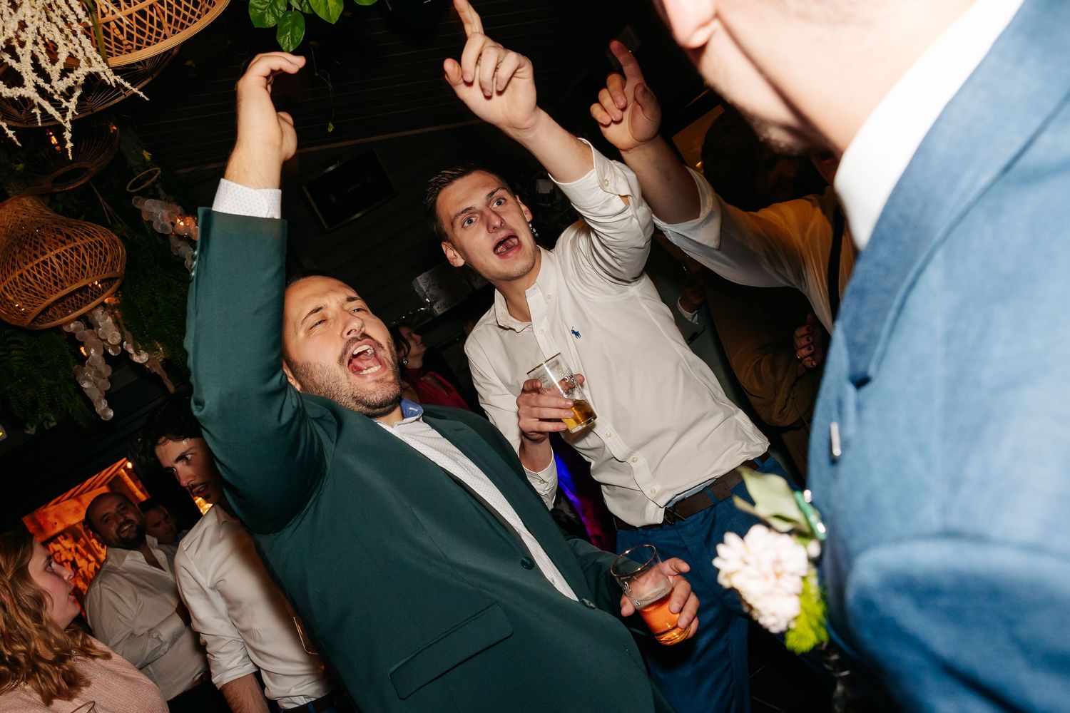 Excited men in suits celebrating and dancing at a wedding reception party.