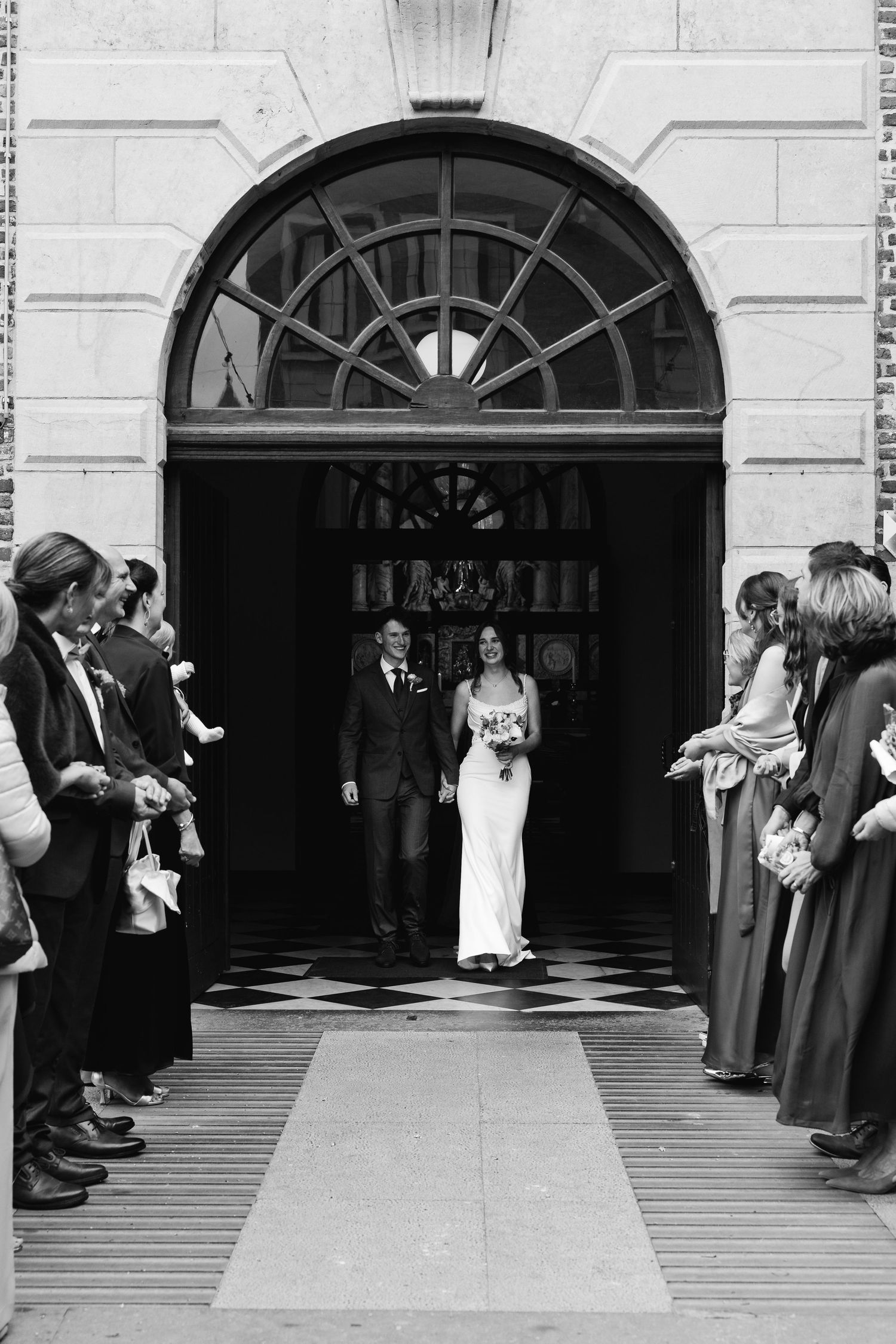Black and white photo of bride and groom walking out of church entrance after ceremony.