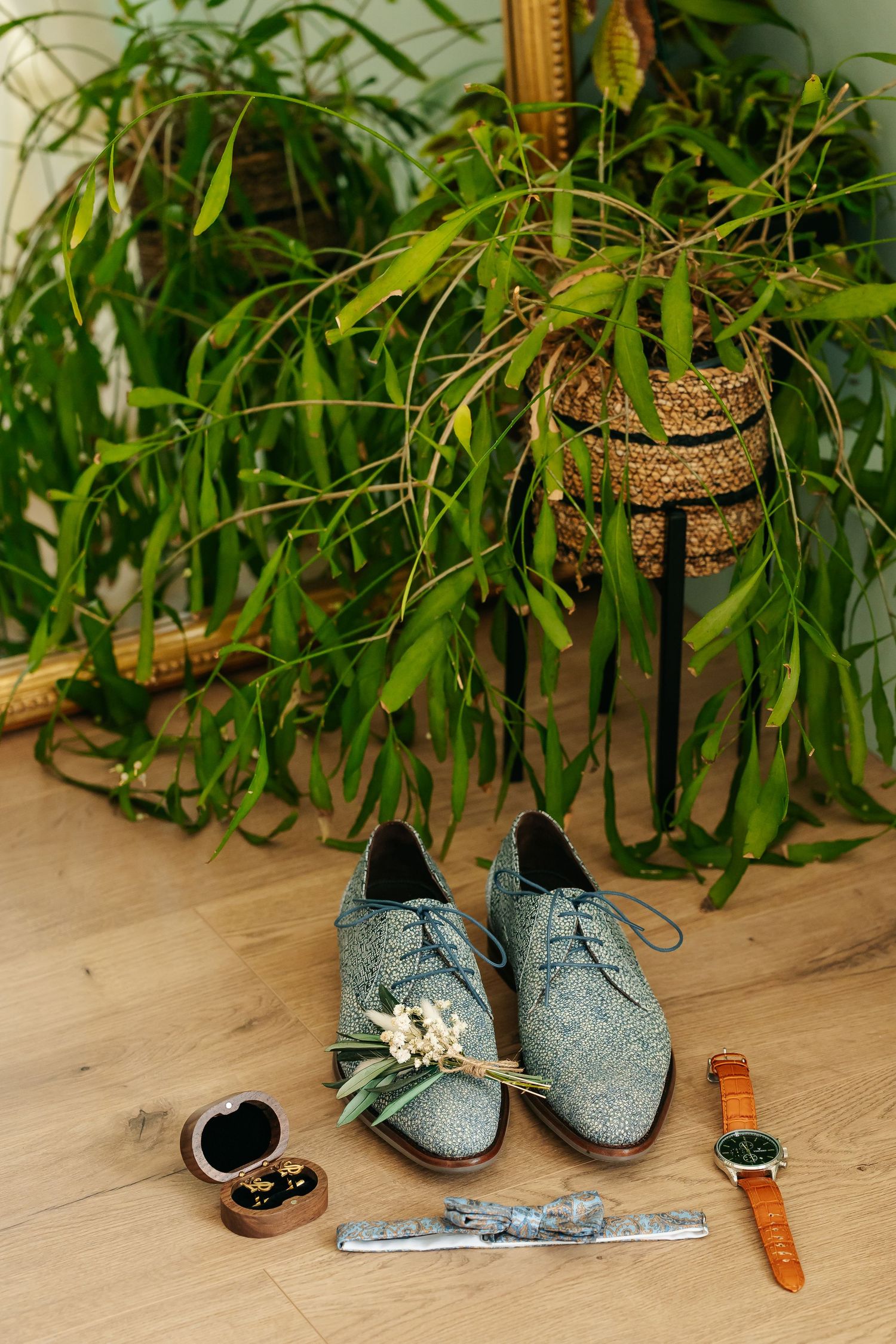 Wedding accessories flat lay with grey suede shoes, boutonniere, watch, cufflinks and tie clip on wood floor.