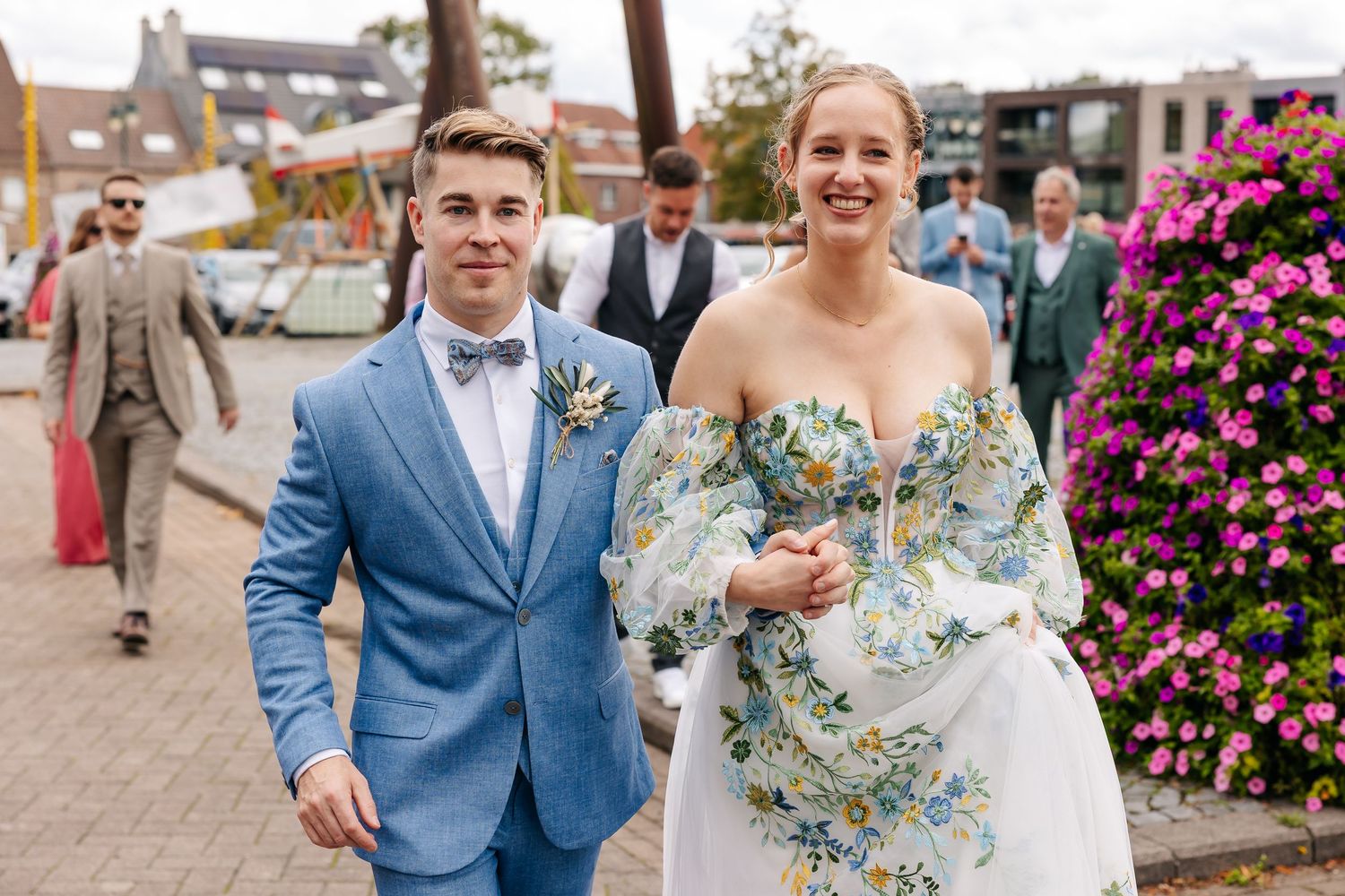 Smiling groom in light blue suit escorts bride in floral dress at wedding.