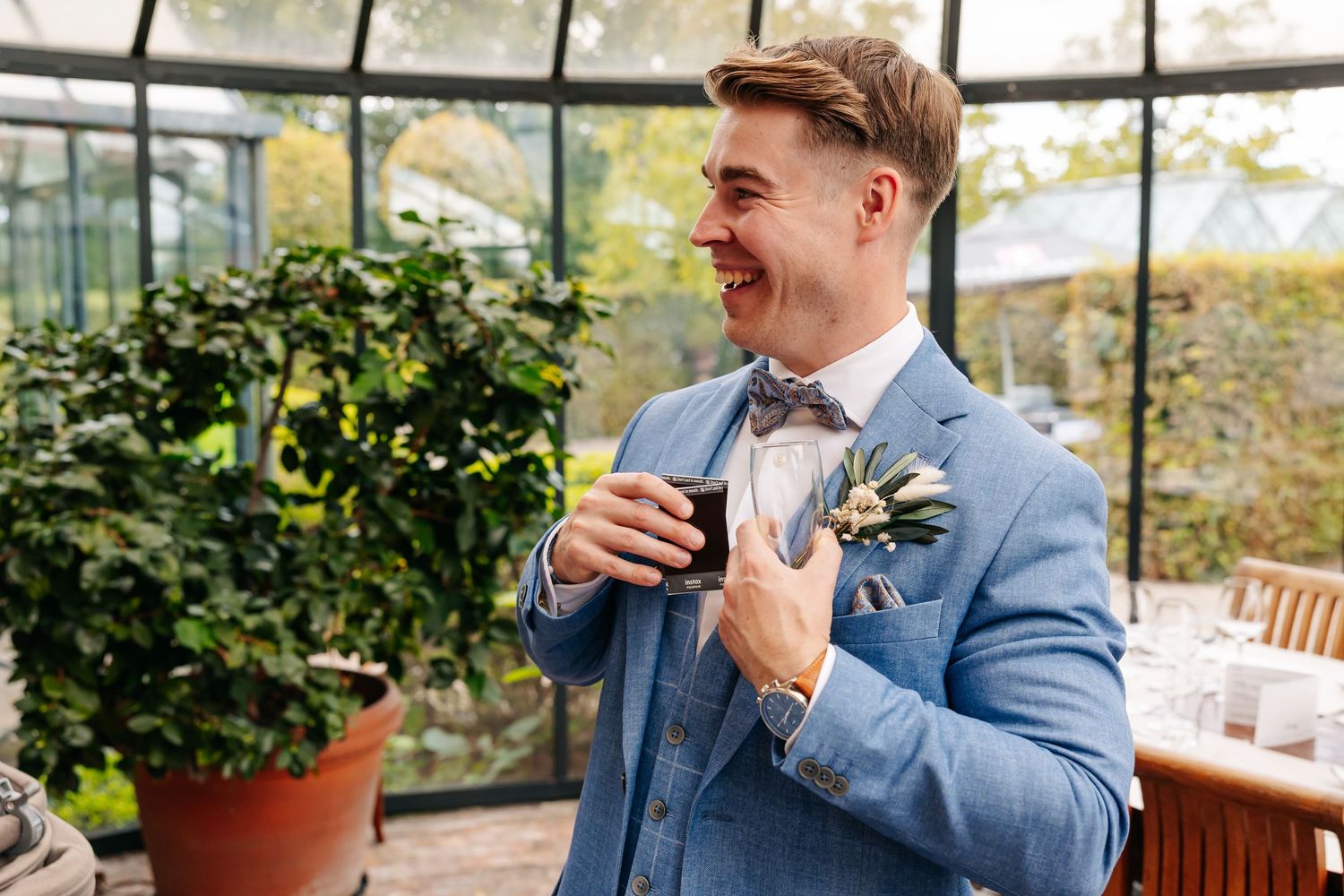 Groom in blue suit with floral boutonniere laughing joyfully at wedding reception.