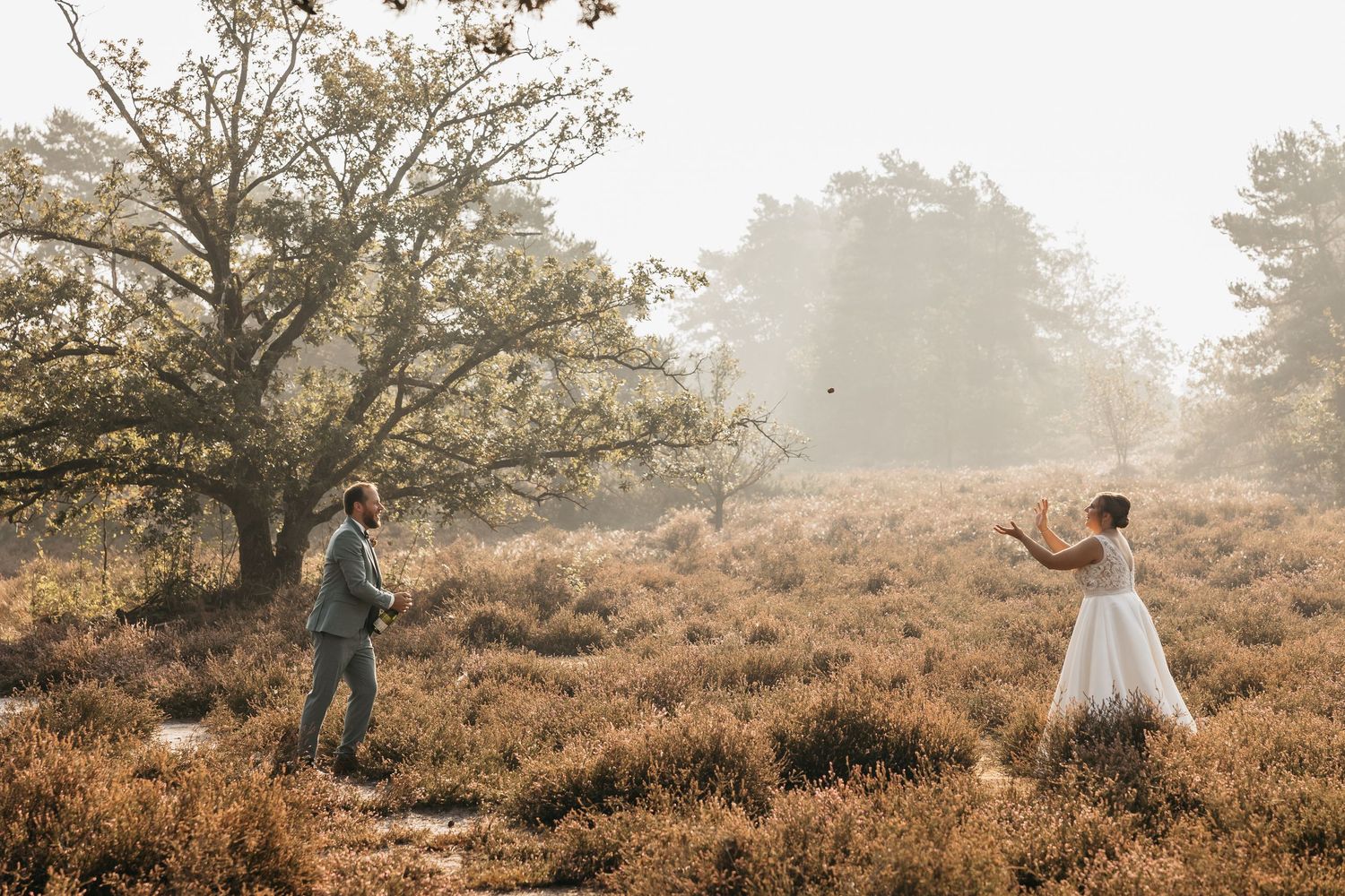 Bride and groom playing catch in misty heathland landscape during outdoor wedding photo session.