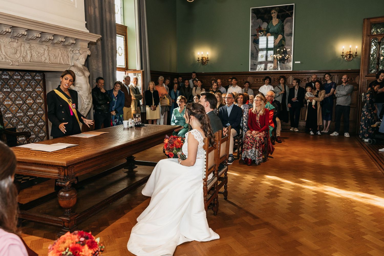 Officiant standing at desk conducting civil wedding ceremony as bride and groom sit before guests.