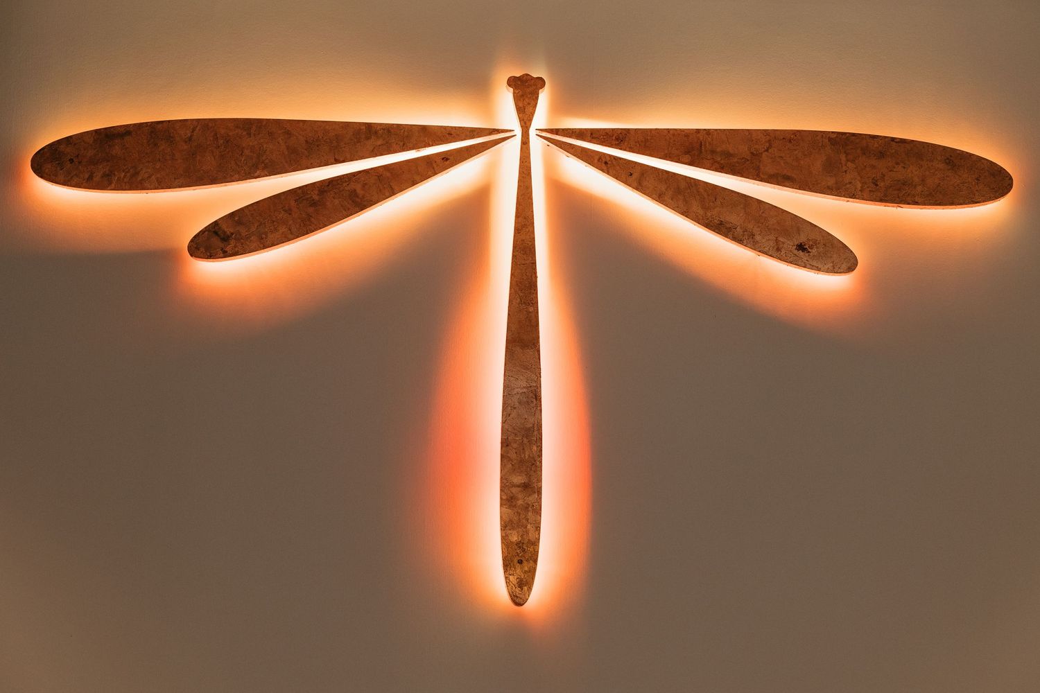 Decorative dragonfly wall art with glowing orange backlight mounted on neutral wall.