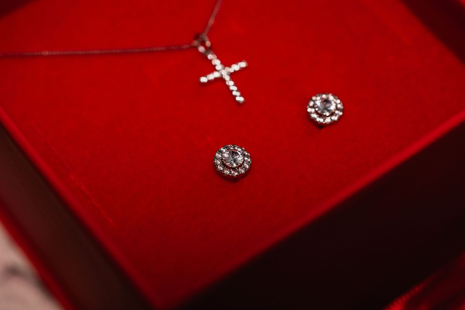 Diamond cross necklace and crystal stud earrings displayed in red velvet jewelry box.