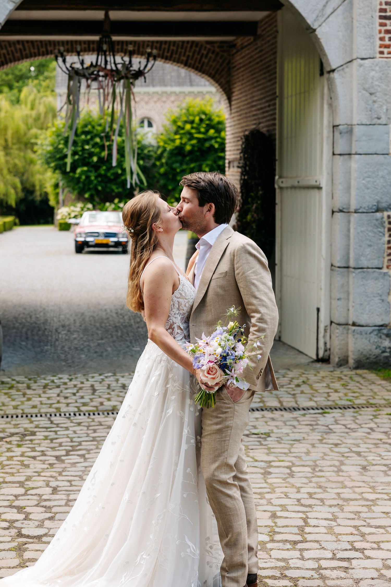 Bride and groom share a kiss under brick archway on cobblestone path.