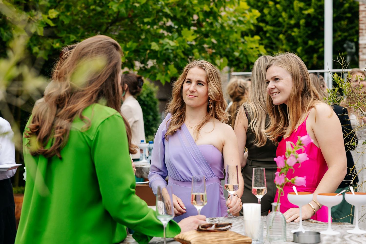 Three women in colorful dresses socializing with wine glasses at an elegant outdoor wedding reception.