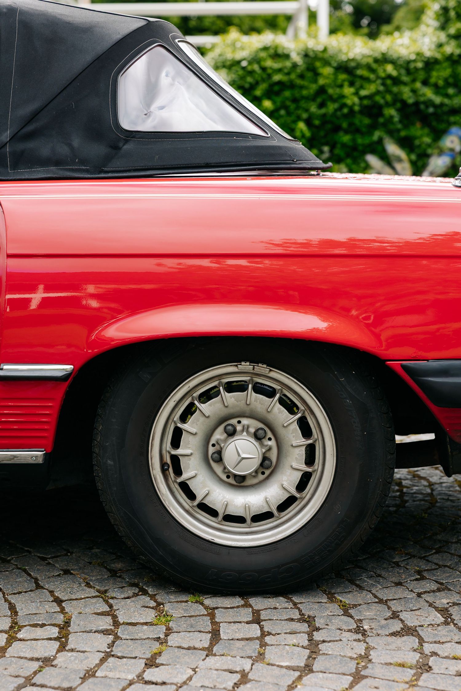 Close-up of a classic red Mercedes-Benz convertible wheel with silver alloy rim on cobblestone.
