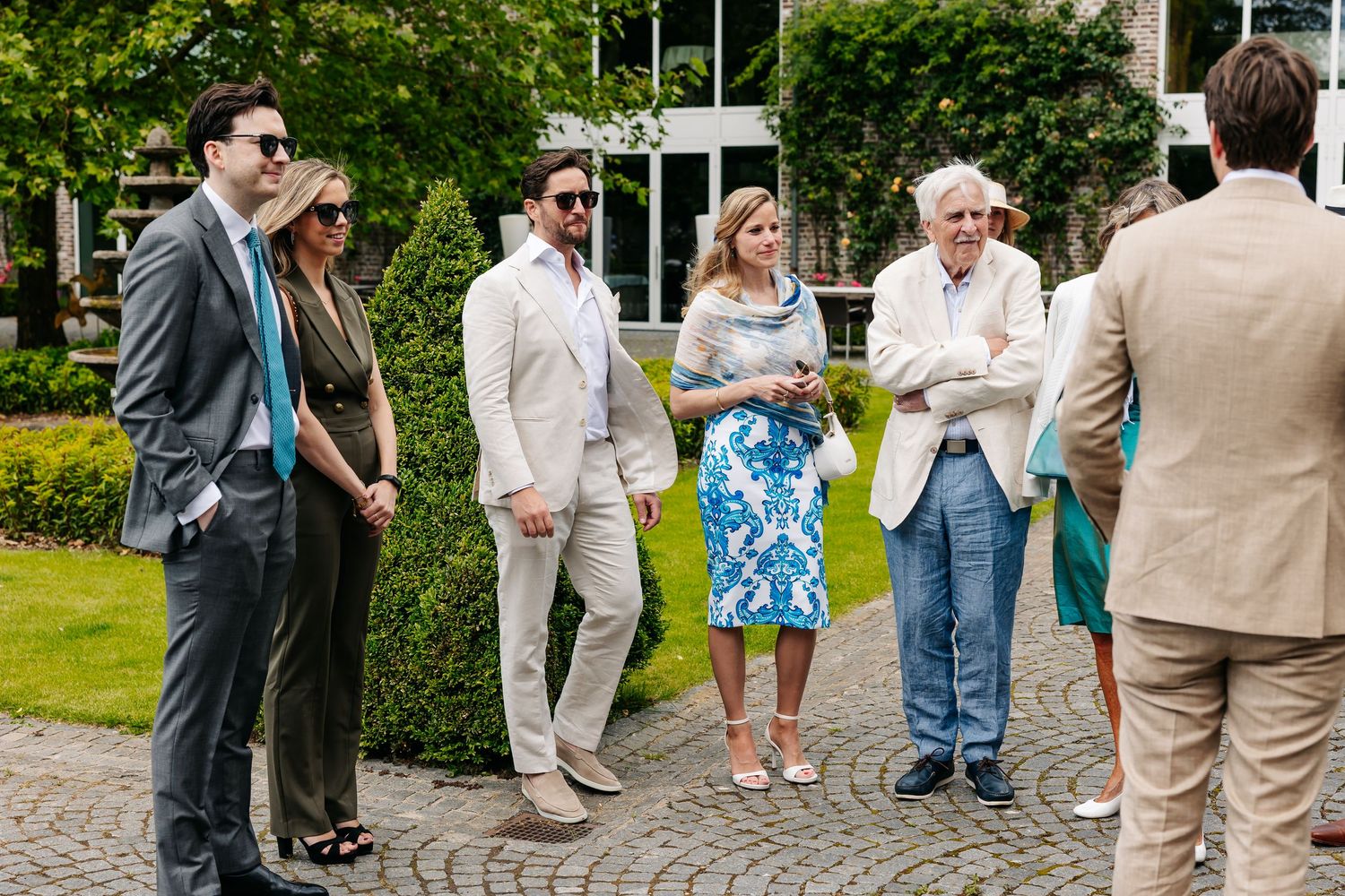 Wedding guests in elegant attire socializing outdoors on cobblestone venue grounds.