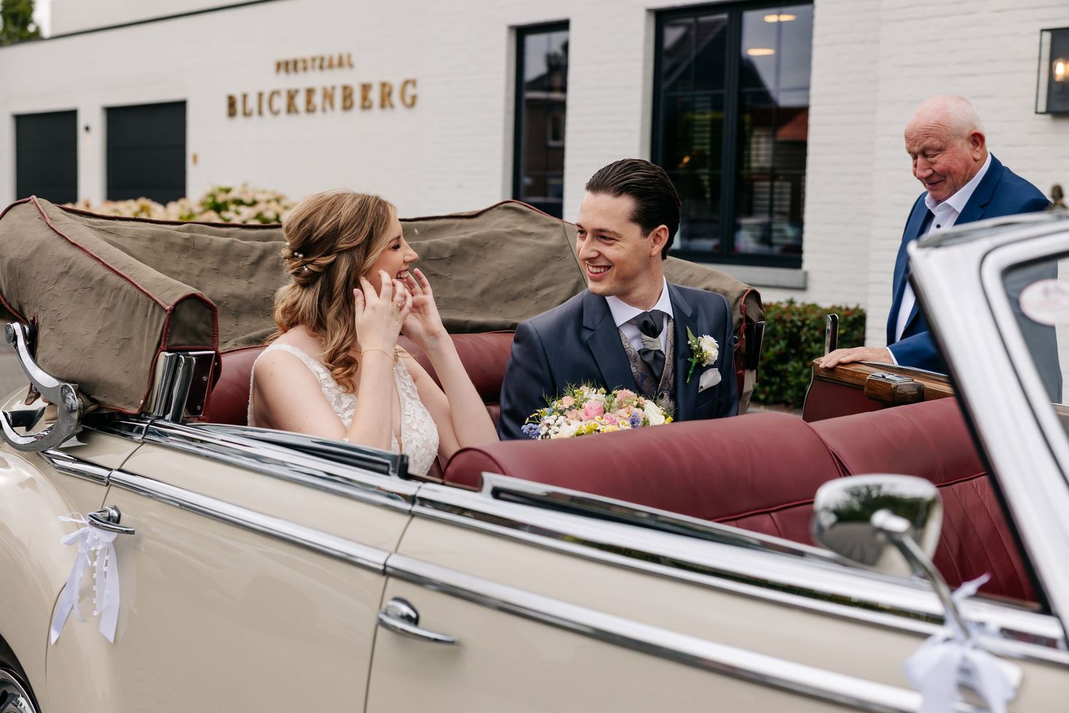Bride and groom sharing a romantic moment in a vintage cream convertible car outside Blickenberg venue.