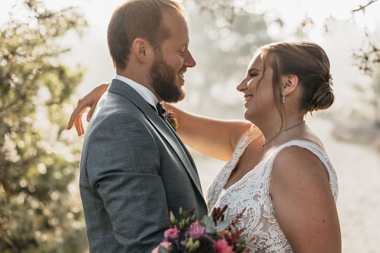 Bride and groom share a tender moment, smiling at each other outdoors.