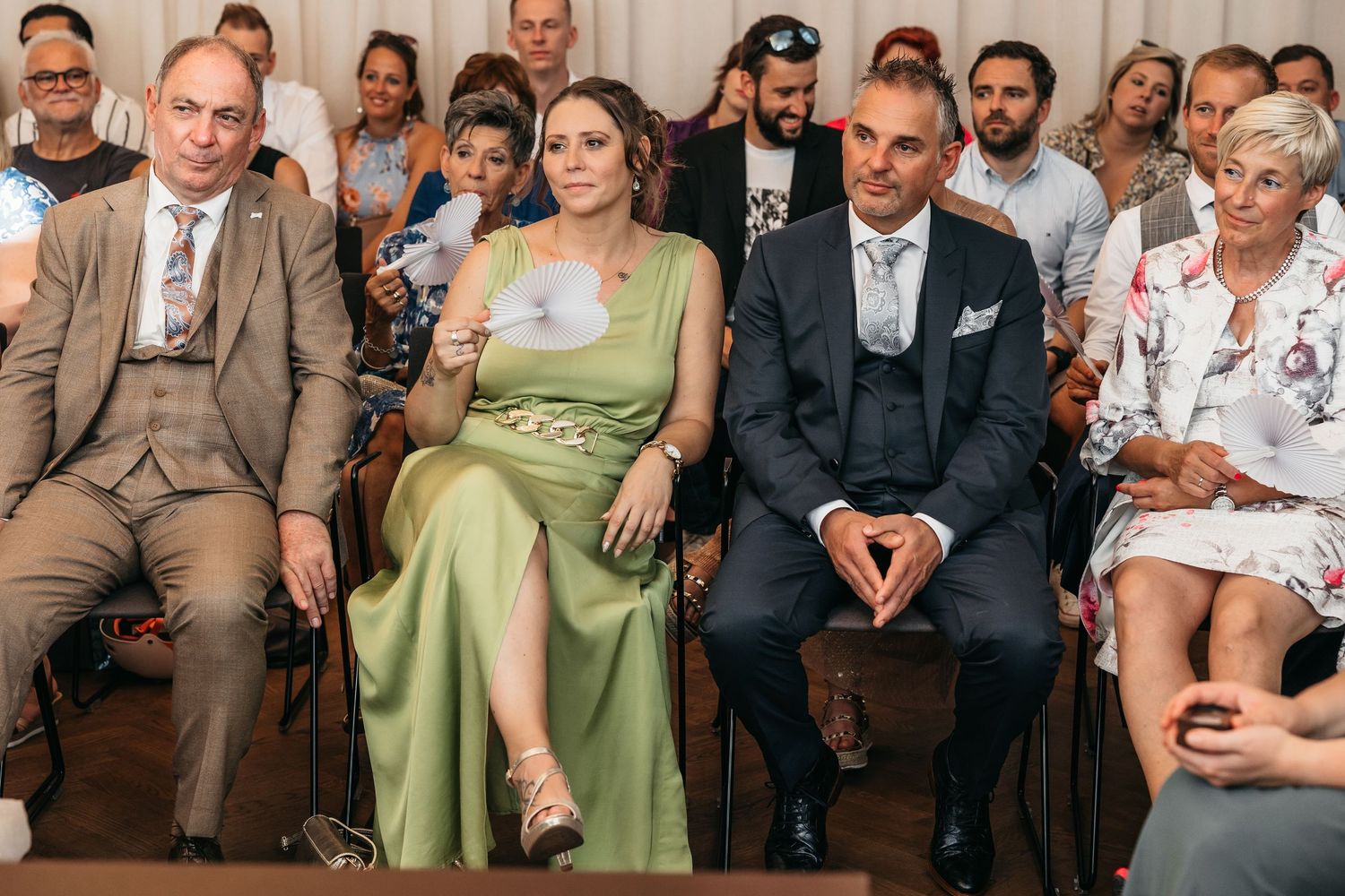 Wedding guests in formal attire including woman in green dress seated during ceremony.