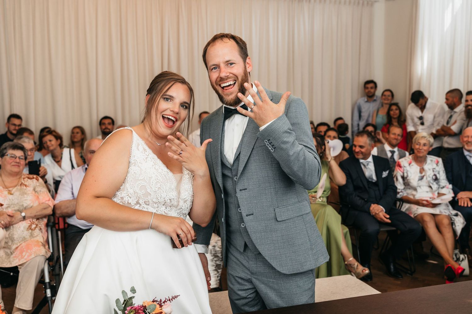 Joyful newlyweds show off their wedding rings to guests after exchanging vows at their ceremony.