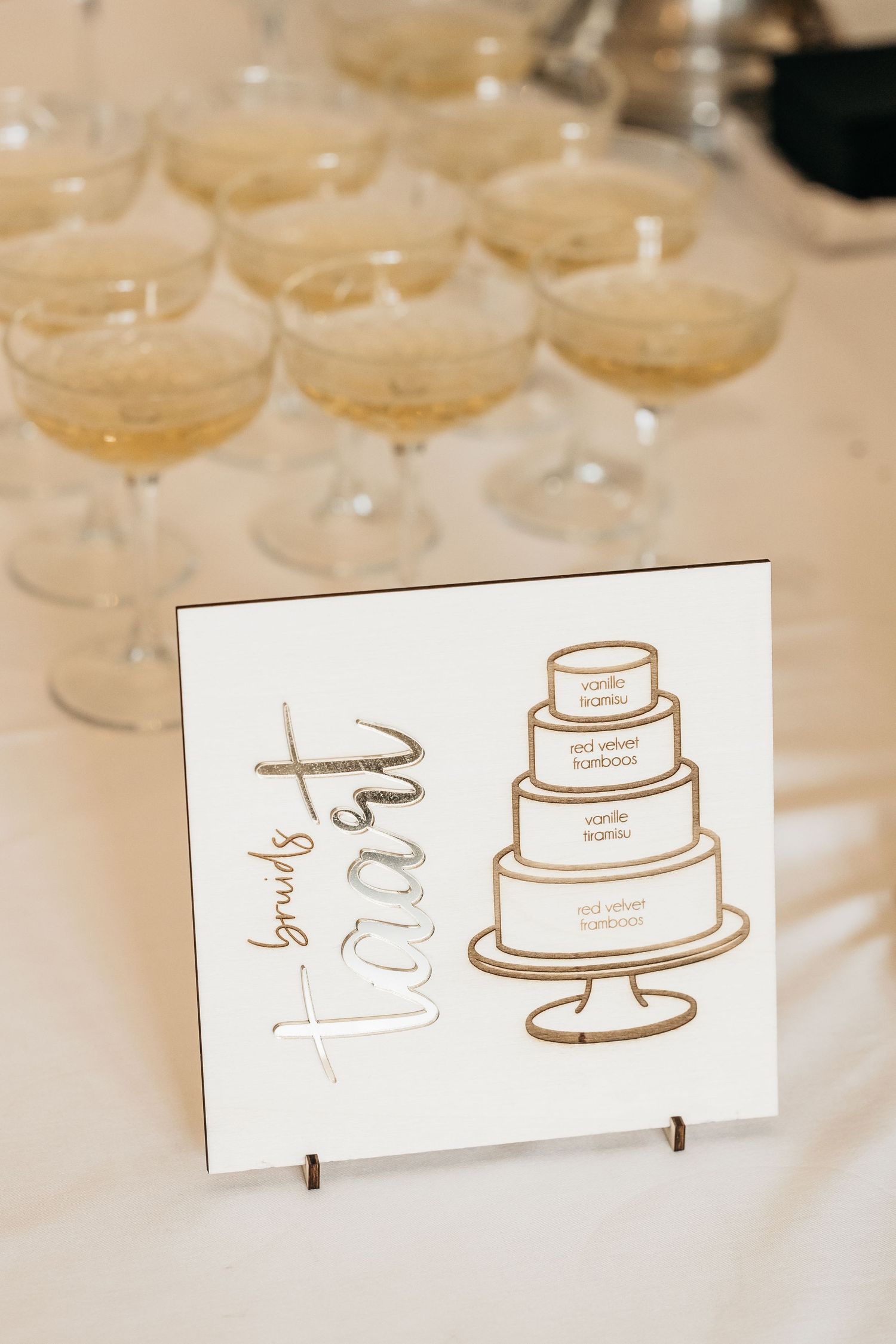 Wedding cake sign reading bruids taart with champagne coupe glasses and a three-tier cake illustration in gold.