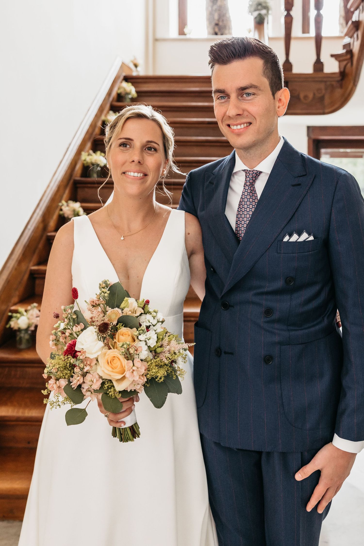 Bride and groom pose together on decorated wooden staircase with bridal bouquet.