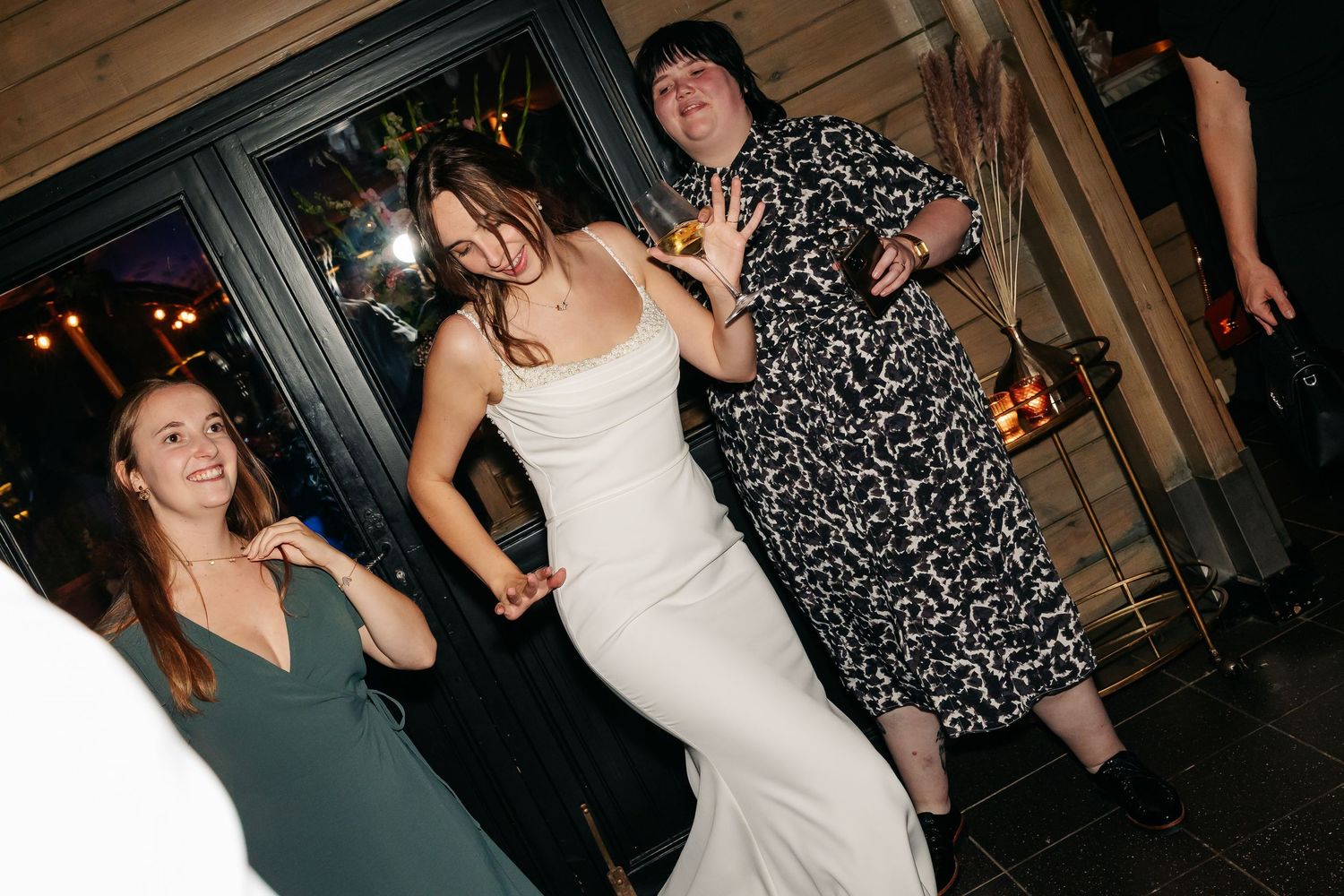 Bride in white gown posing and dancing with guests outside wedding venue at night.