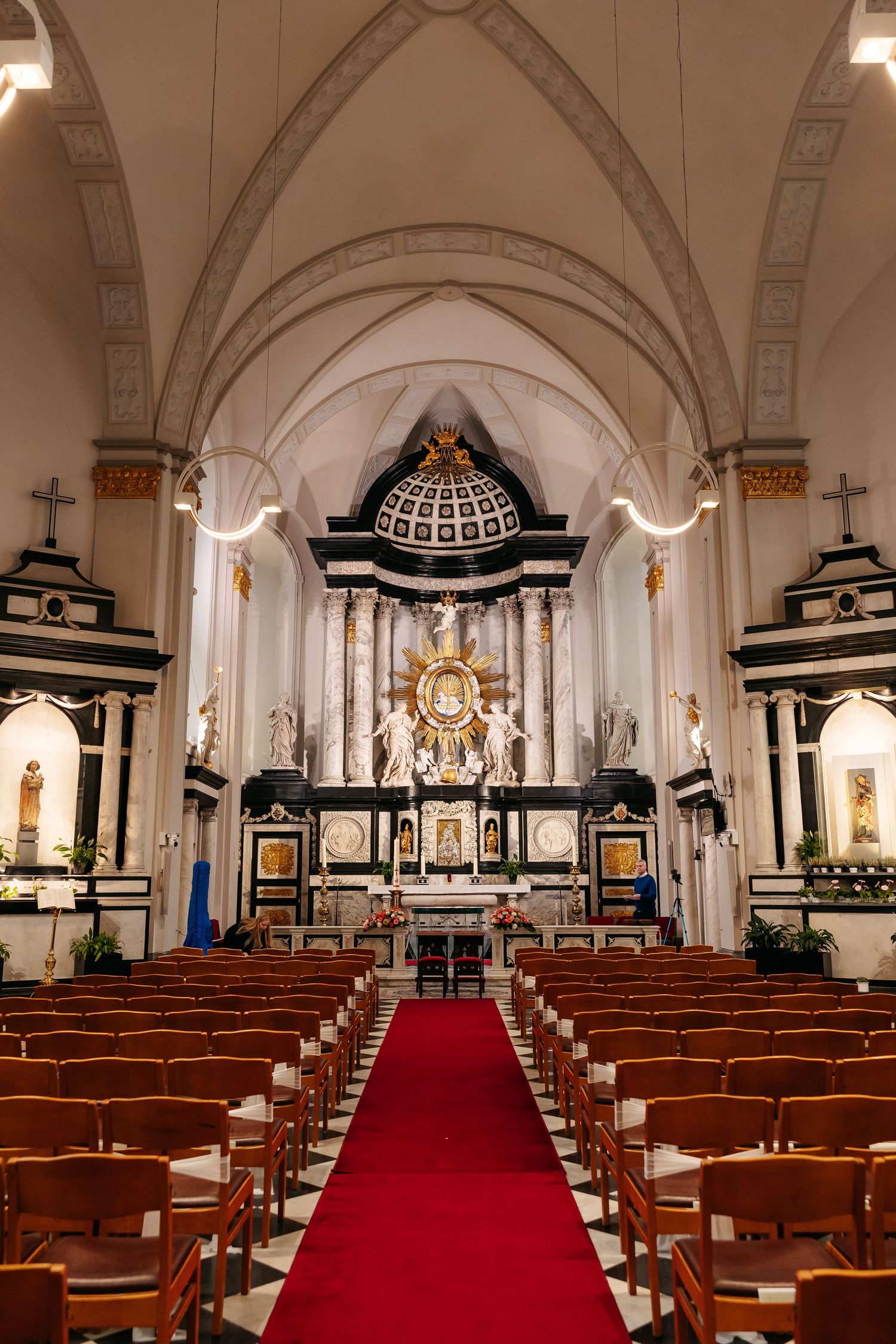 Elegant Catholic church interior with red carpet aisle, ornate altar, and wooden pews.