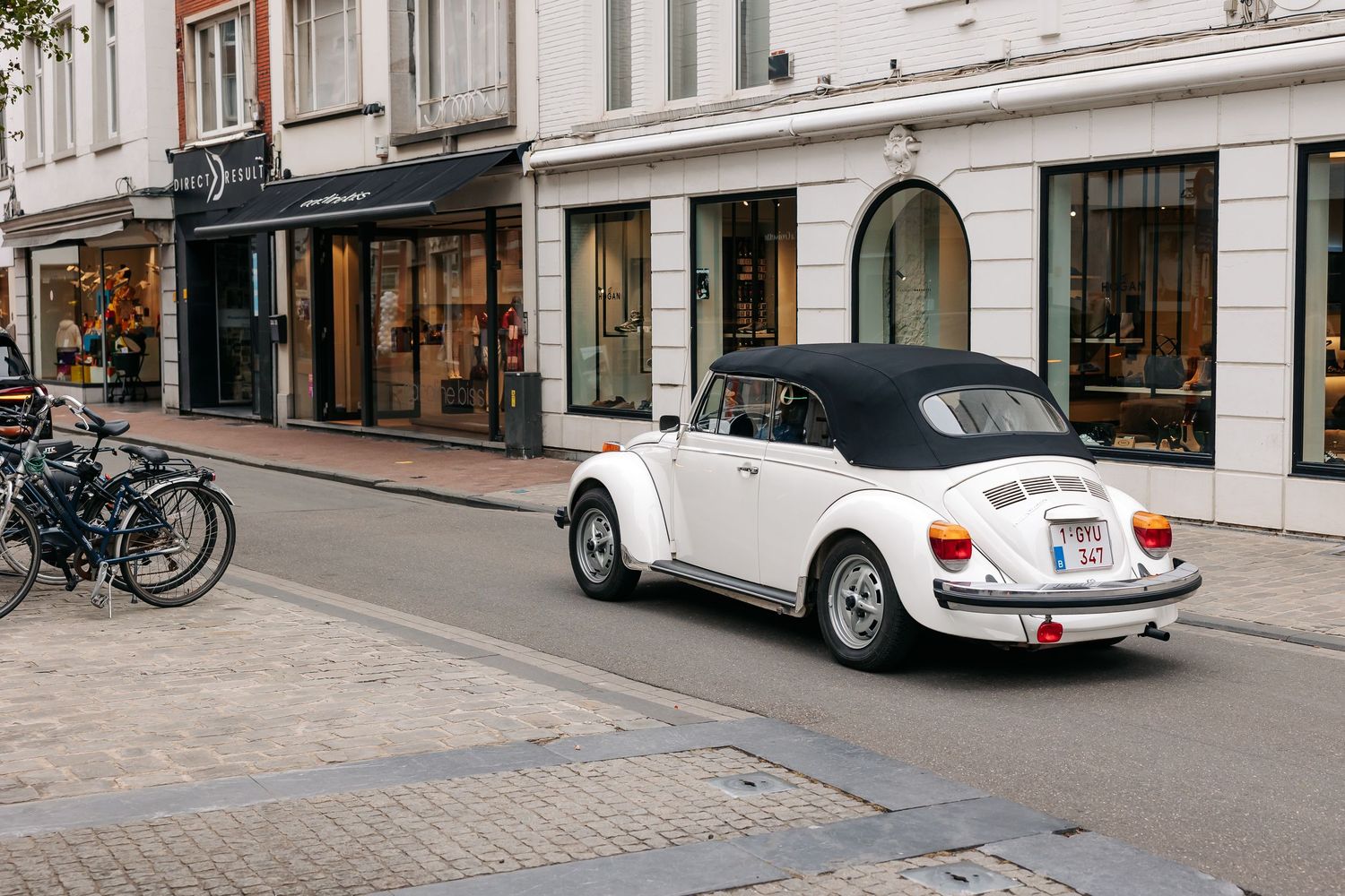 Classic white Volkswagen Beetle convertible drives down a charming European city street on a wedding day.