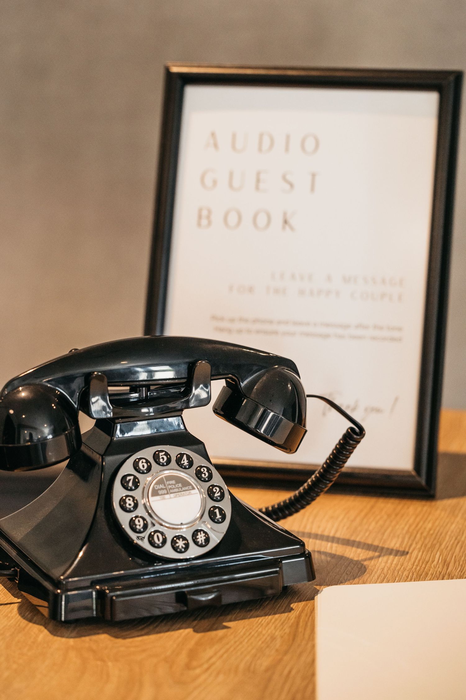 Vintage black rotary phone beside a framed audio guest book sign at a wedding reception.
