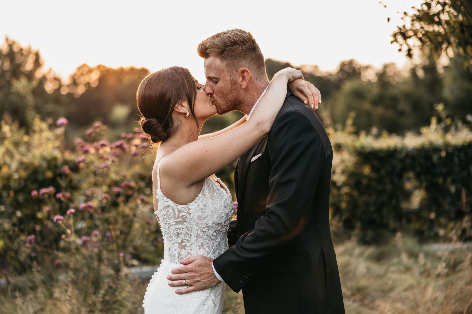 Bride and groom sharing a romantic kiss at golden hour outdoors.