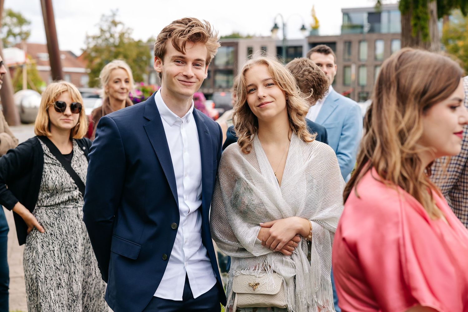 Young couple poses together at outdoor wedding, man in navy suit, woman in silver wrap.