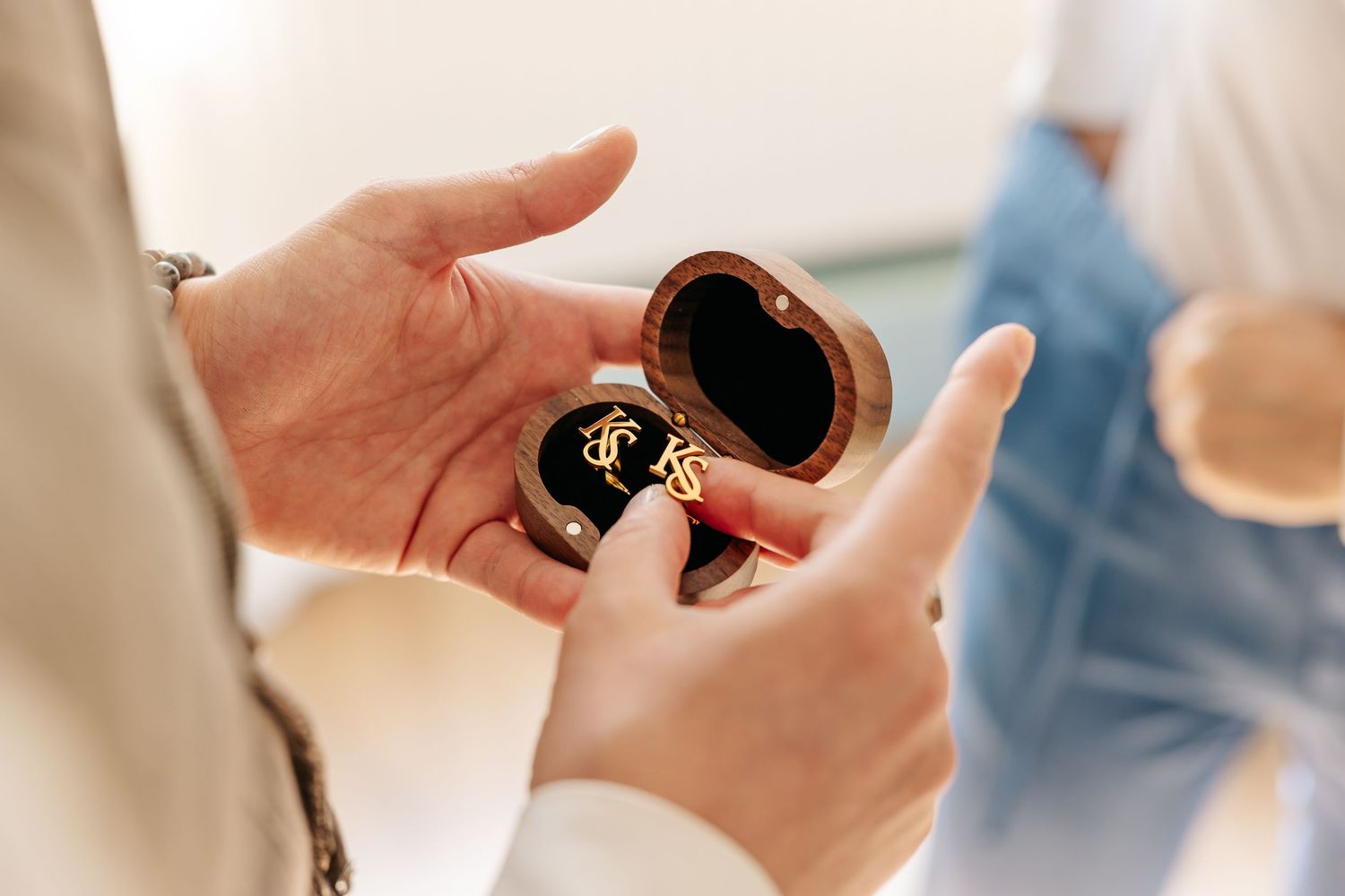 Hands holding open heart-shaped wooden ring box with gold wedding rings inside.