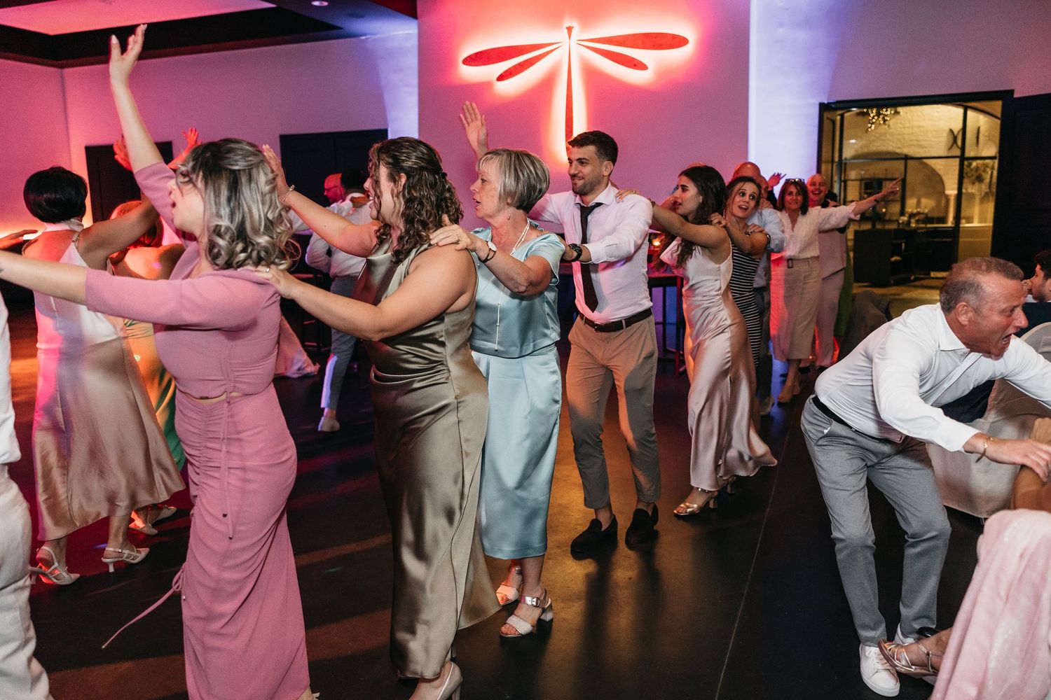 Guests dancing energetically at a wedding reception with pink neon lighting and a lively atmosphere.