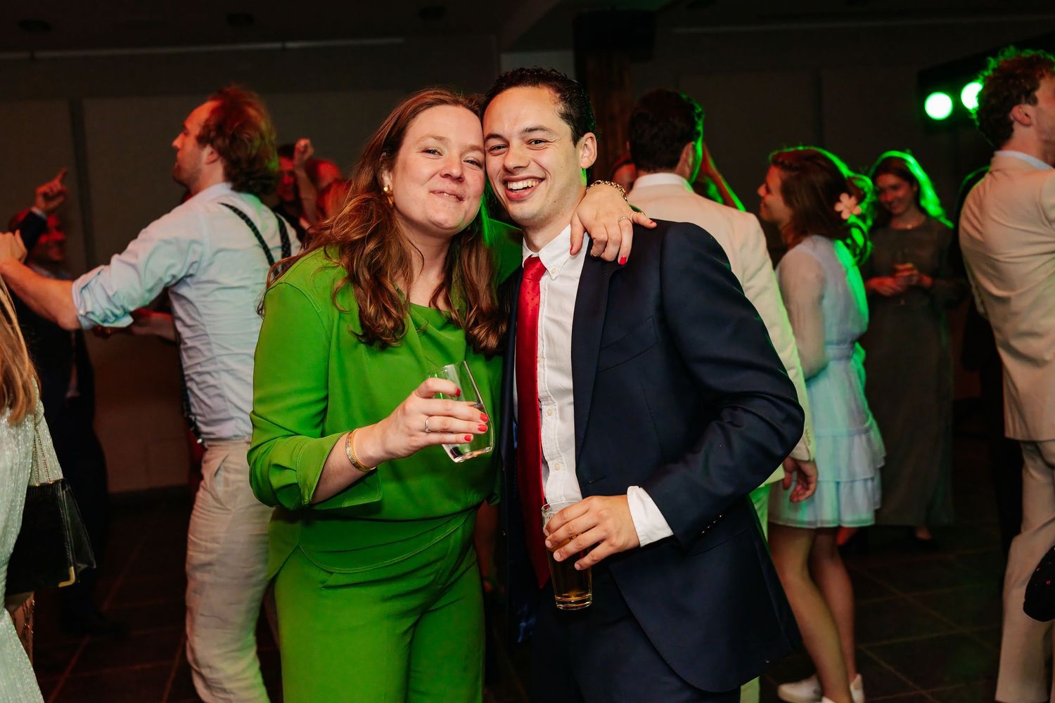 Woman in green dress and man in blue suit posing together at a wedding dance party.
