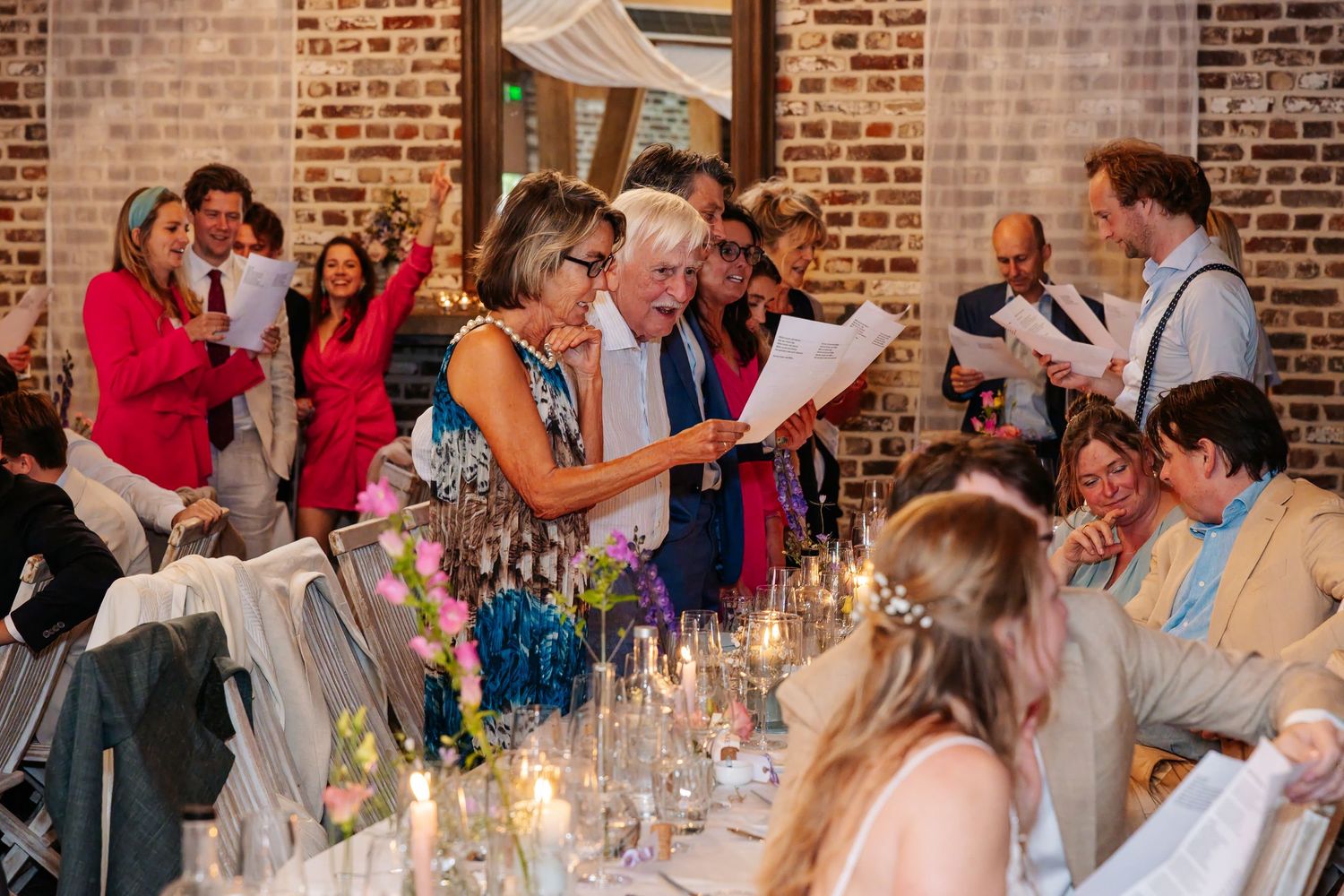 Wedding guests singing and celebrating together at a candlelit reception dinner table.