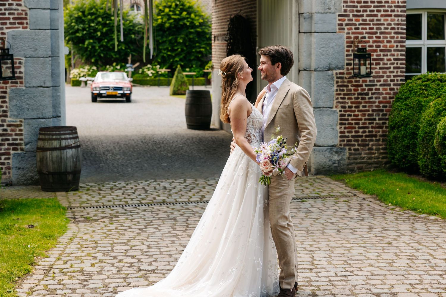 Bride and groom share a romantic moment on a cobblestone driveway outside a charming brick estate.