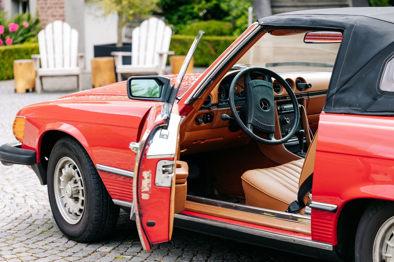 Red classic Mercedes-Benz convertible with open door revealing tan leather interior, parked on cobblestone driveway.