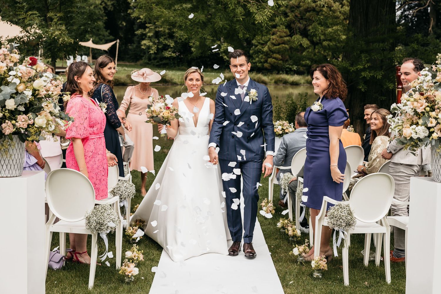 Newlyweds walking down aisle as guests throw flower petals at outdoor garden wedding.