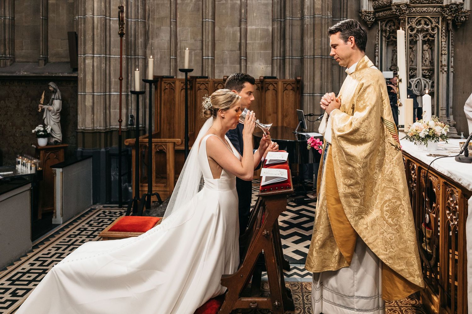 Bride receiving communion from priest at ornate church altar during Catholic wedding ceremony.