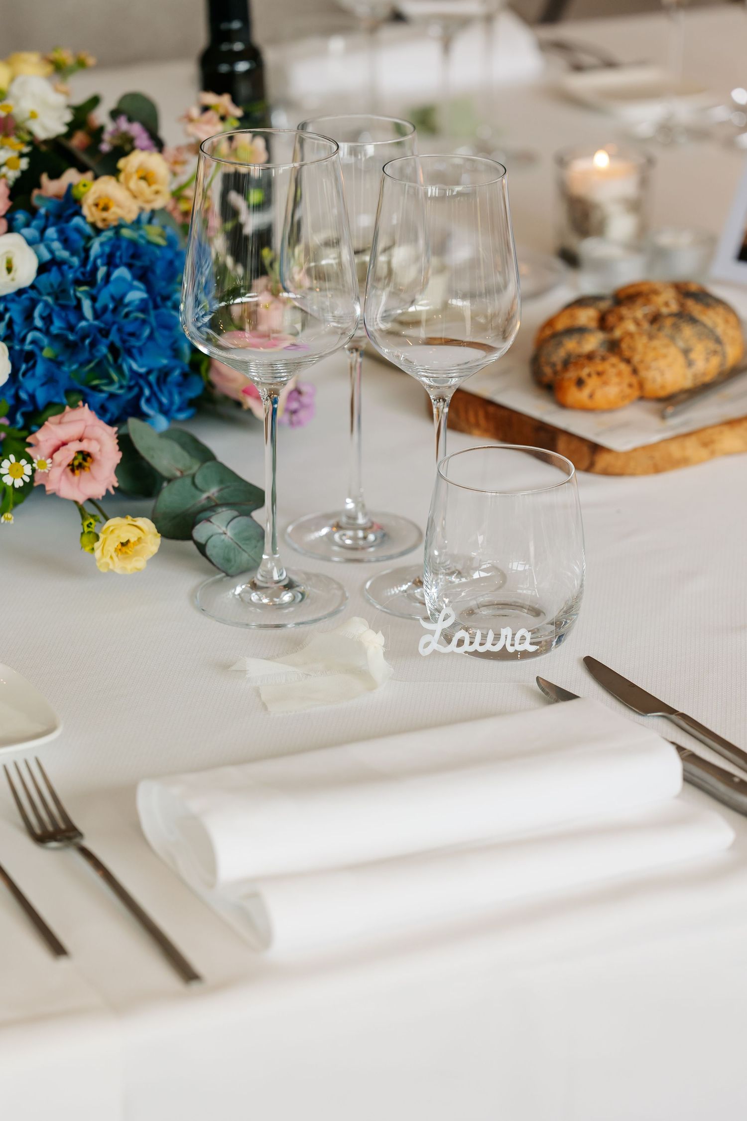 Wedding reception place setting with crystal wine glasses, white napkin, and a laser-cut name card reading Laura.