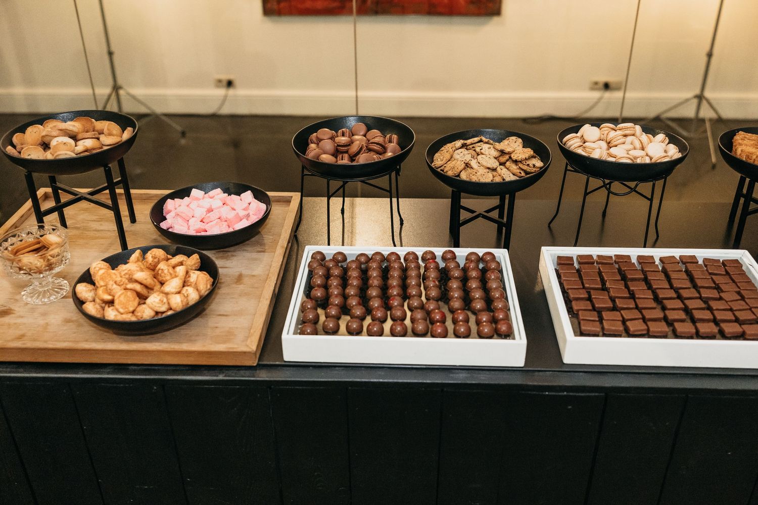 Wedding dessert table displaying assorted chocolates, macarons, marshmallows, and sweet treats on black stands.