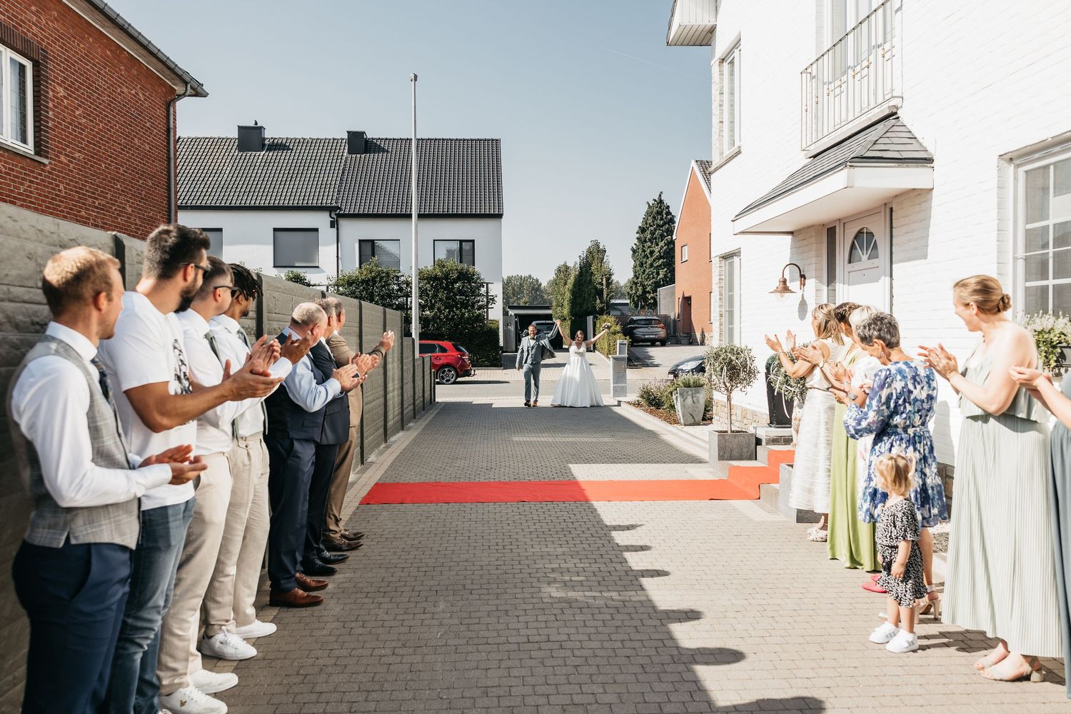 Wedding guests line a red carpet path applauding as the newlyweds make their grand outdoor entrance.