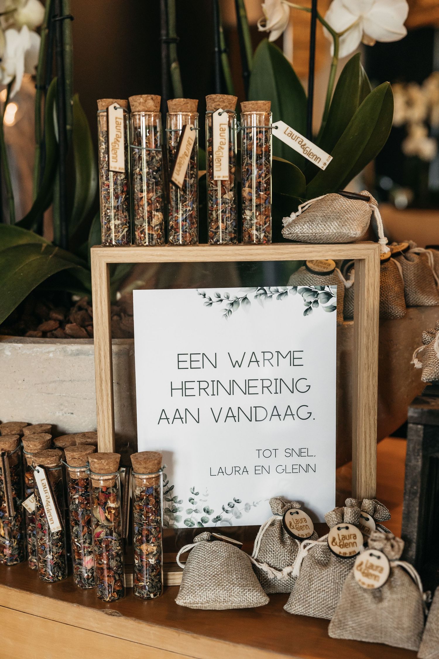 Wedding favor display with herb-filled test tubes and linen bags beside a Dutch sign from Laura and Glenn.