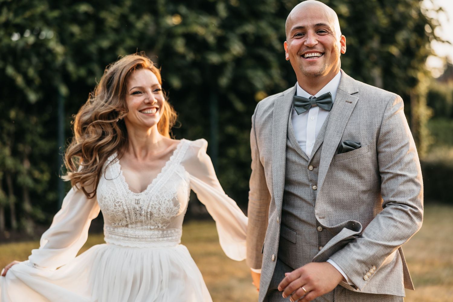 Happy bride and groom walking hand in hand outdoors in golden hour light at their wedding celebration.
