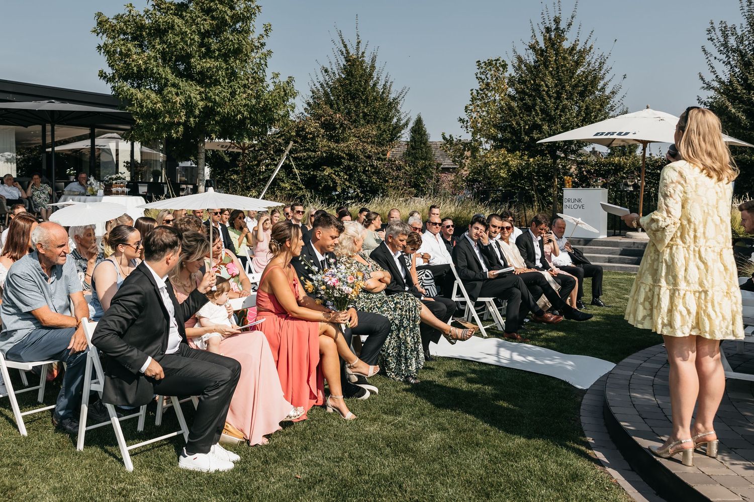 Officiant addresses seated wedding guests during elegant outdoor garden ceremony on sunny day.