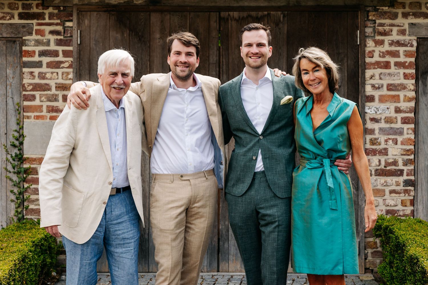 Happy family of four posing together outdoors at a wedding celebration near a rustic brick wall.