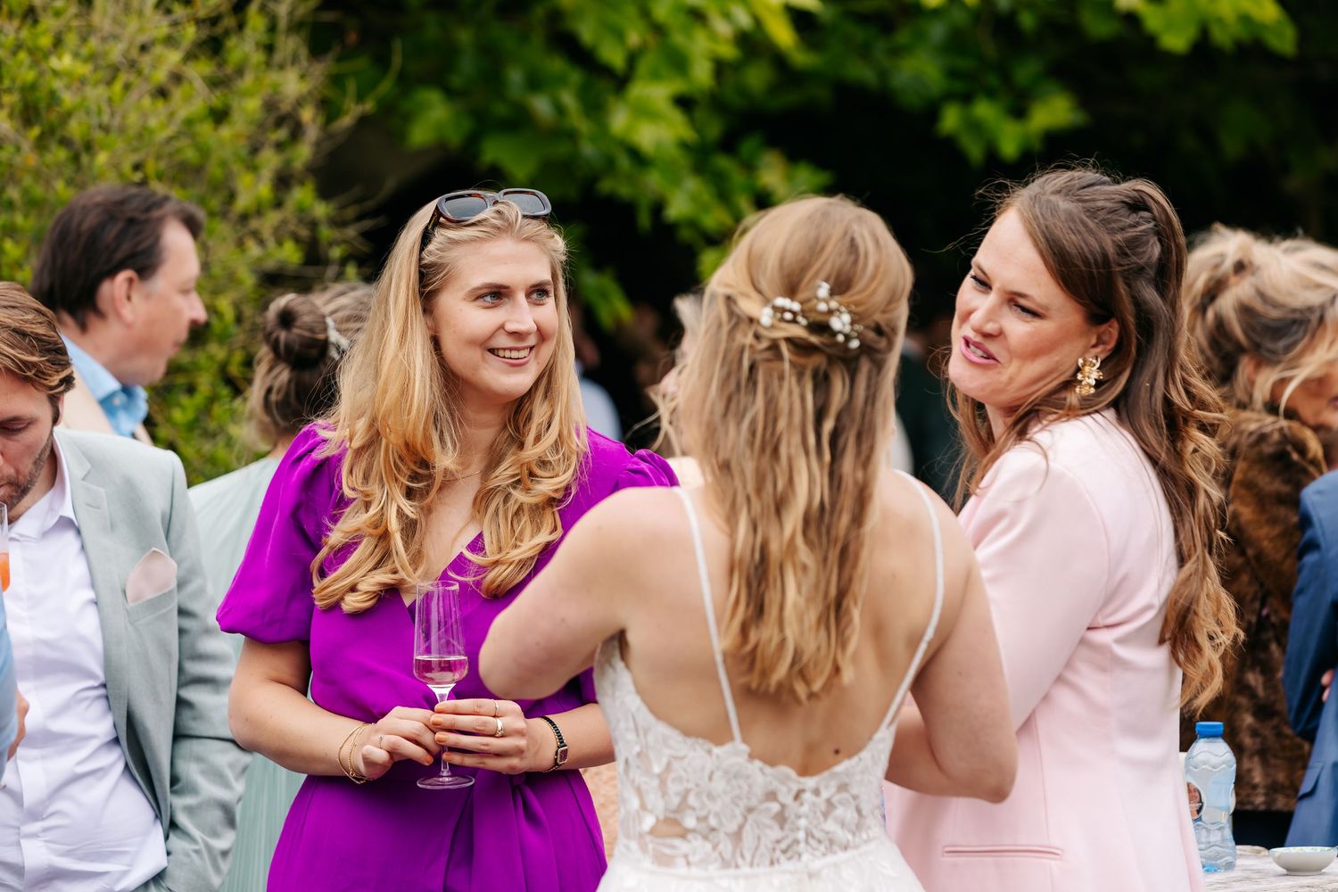 Wedding guests in colorful dresses laugh and chat together at an outdoor reception.