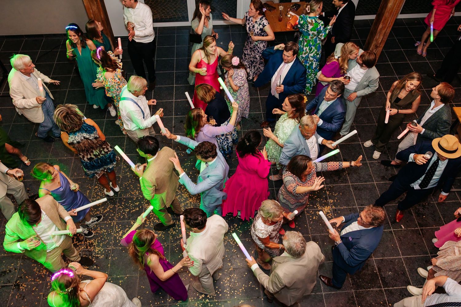 Aerial view of wedding guests dancing with light-up batons on decorated dance floor.