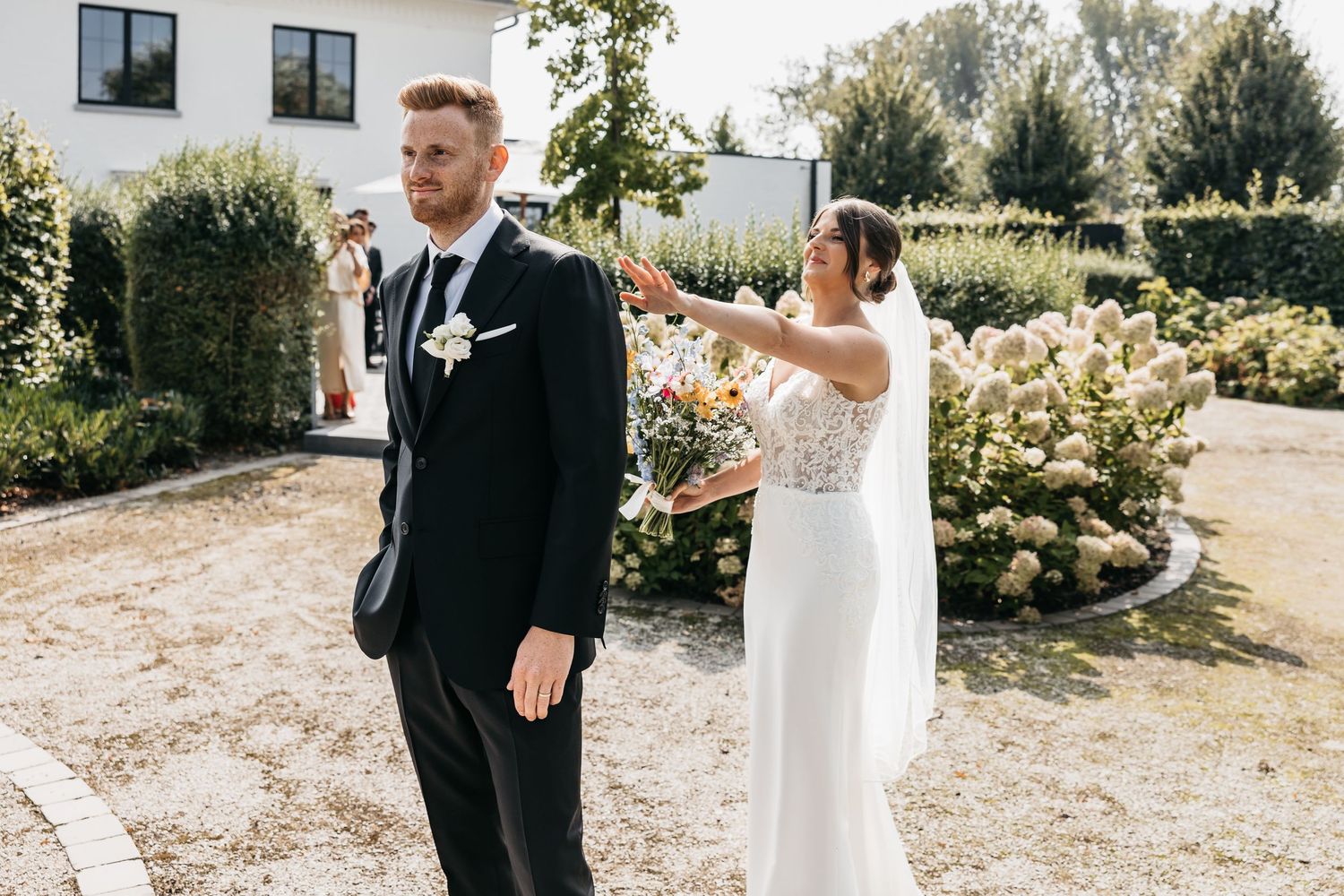 Bride in white gown tapping groom in black suit on shoulder during first look moment.